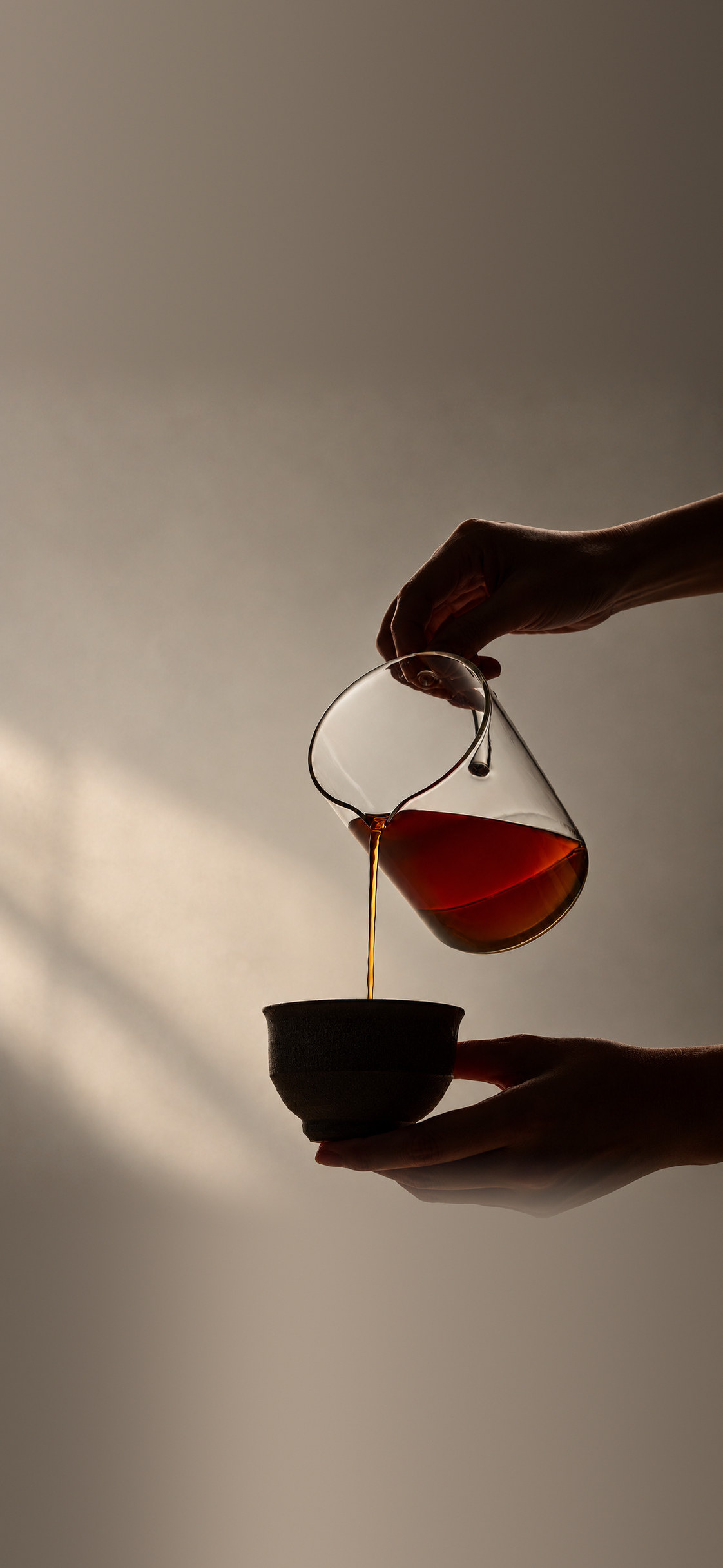 Coffee poured from a glass server into a cup held in two hands