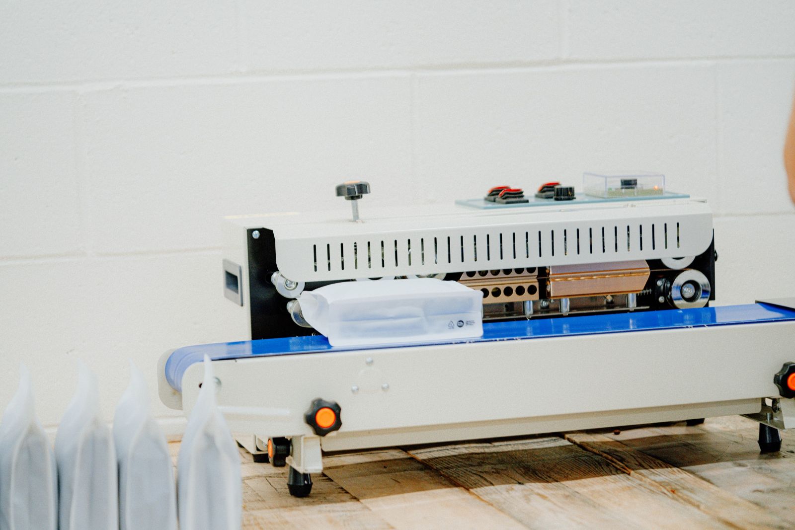 A bag of coffee going through the band sealer on its blue conveyor, with sealed bags lined up beside it